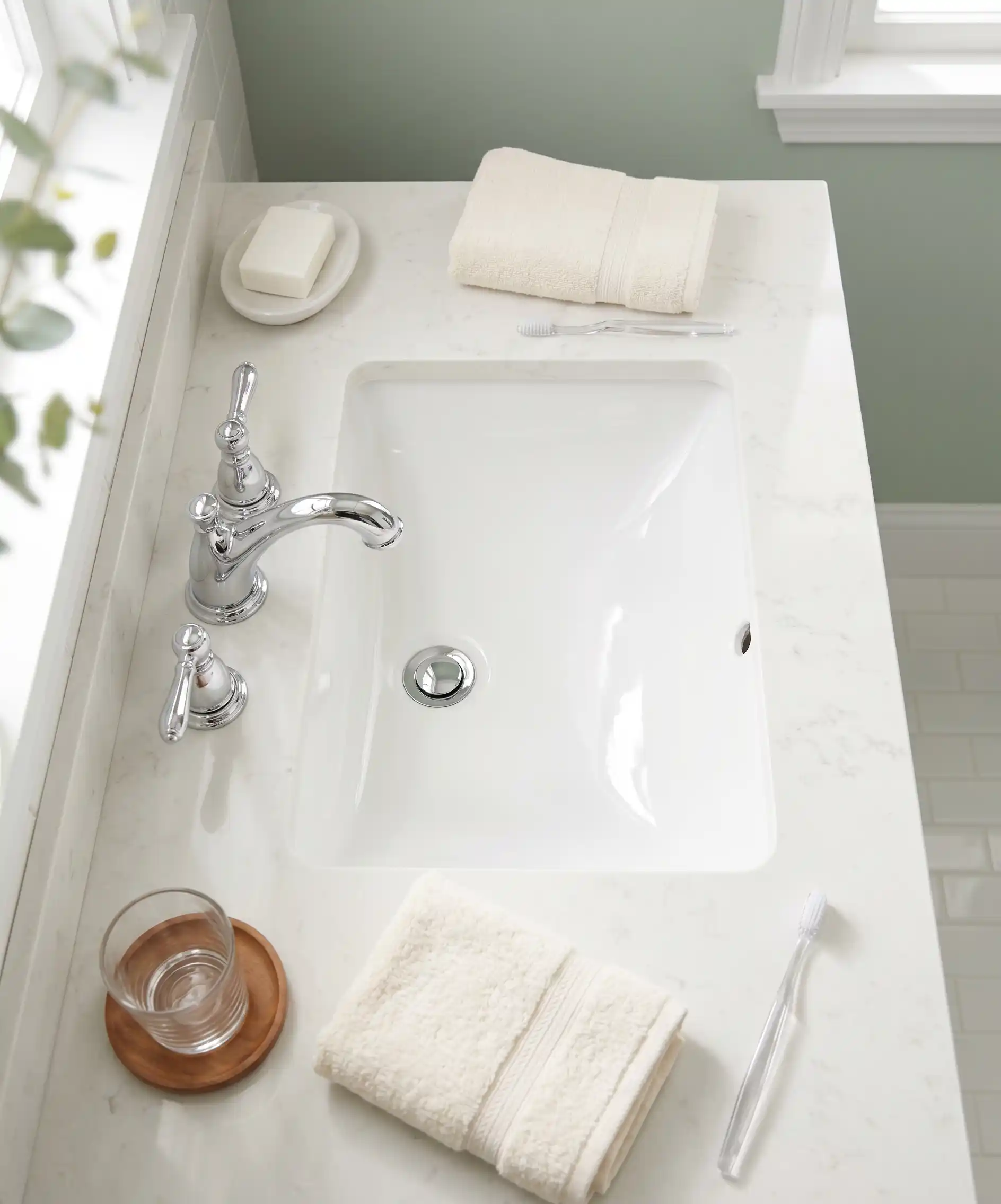 A bright, clean bathroom sink photo from above — gleaming white porcelain, clean faucet handles, a neatly folded hand towel to the side, no toothpaste residue or water spots — the 30-second wipe result.
